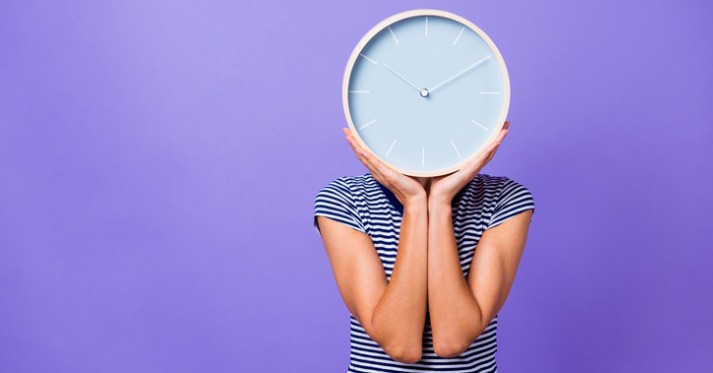 woman in a striped shirt holding a wall clock in front of her face