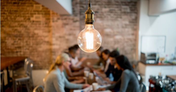 Group of people brainstorming at a creative office and a light bulb in the foreground