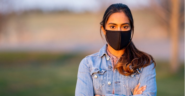 hispanic woman in a black face mask and a denim jacket looking at the camera