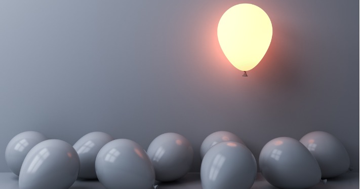 One light balloon glowing and floating above other white balloons on white wall background with window reflections and shadows